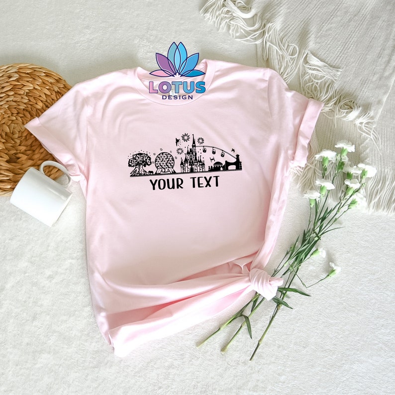 K&ouml;nnte beinhalten: Rosa T-Shirt mit einer schwarzen Silhouette der Disney World Skyline, einschlie&szlig;lich Cinderella's Castle, Spaceship Earth und dem ikonischen Bahnhof. Der Text "YOUR TEXT" ist unterhalb der Skyline gedruckt.