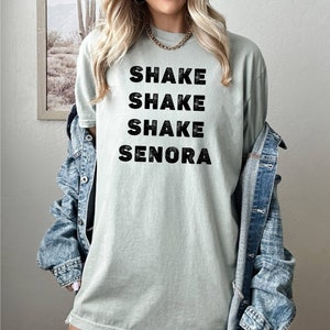 May include: A light green t-shirt with the text "Shake Shake Shake Senora" printed in black.