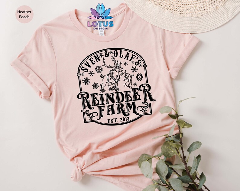 May include: A pink t-shirt with a black graphic design featuring a reindeer and a snowman with the text "Sven & Olaf's Reindeer Farm Est. 2013".
