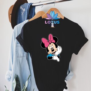 K&ouml;nnte beinhalten: Schwarzes T-Shirt mit einem Cartoon-Bild von Minnie Mouse, die eine rosa Schleife tr&auml;gt. Der Text "LOTUS DESIGN" ist auf dem Shirt aufgedruckt.