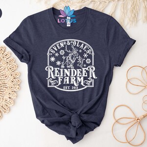 May include: A navy blue t-shirt with a white graphic design featuring a reindeer with the text "Sven & Olaf's Reindeer Farm Est. 2013".