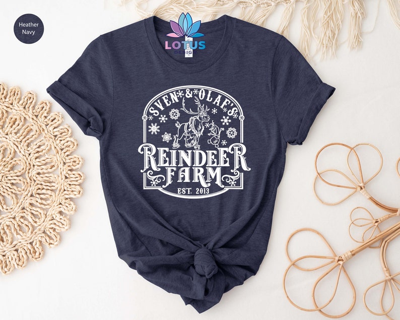 May include: A navy blue t-shirt with a white graphic design featuring a reindeer with the text "Sven & Olaf's Reindeer Farm Est. 2013".