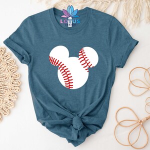 May include: A teal blue t-shirt with a white baseball-shaped Mickey Mouse head graphic. The baseball has red stitching.