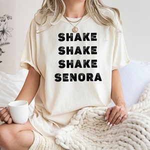 May include: A white t-shirt with the text "Shake Shake Shake Senora" printed in black.