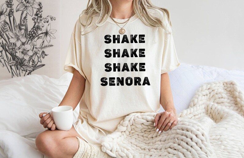 May include: A white t-shirt with the text "Shake Shake Shake Senora" printed in black.