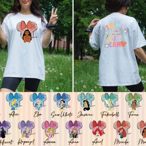 Puede incluir: Camiseta blanca con un gr&aacute;fico de una princesa Disney con una diadema de Minnie Mouse. La parte posterior de la camiseta dice "I'm in my Disney Era" con orejas y manos de Mickey Mouse. Hay 12 gr&aacute;ficos diferentes de princesas Disney en una cuadr&iacute;cula debajo de la camiseta.
