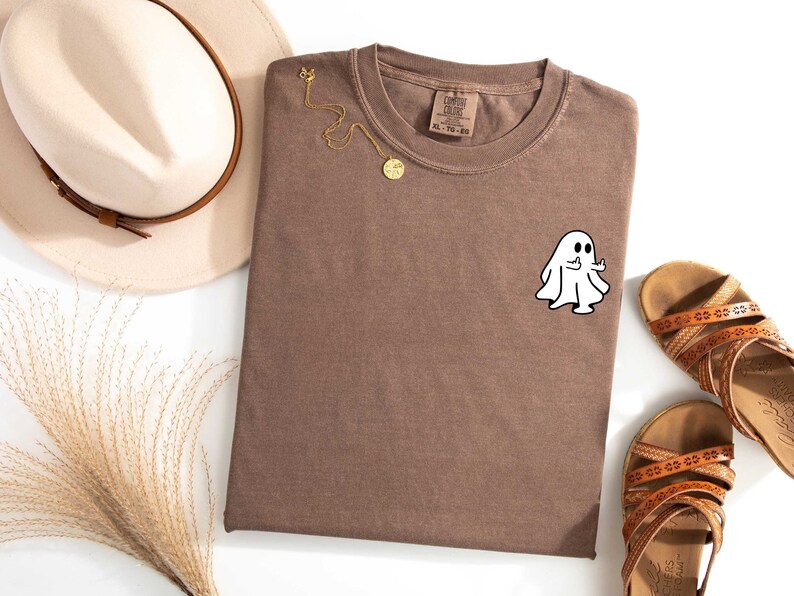 May include: A brown t-shirt with a white ghost giving a thumbs up. The ghost is on the left side of the shirt.