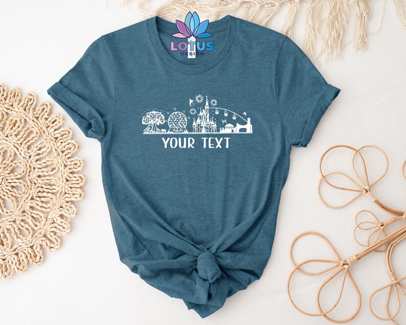 K&ouml;nnte beinhalten: Ein blaues T-Shirt mit einem wei&szlig;en Umriss der Disney World Skyline, einschlie&szlig;lich Cinderella's Castle, Spaceship Earth und dem Haunted Mansion. Der Text "YOUR TEXT" ist unterhalb der Skyline gedruckt.