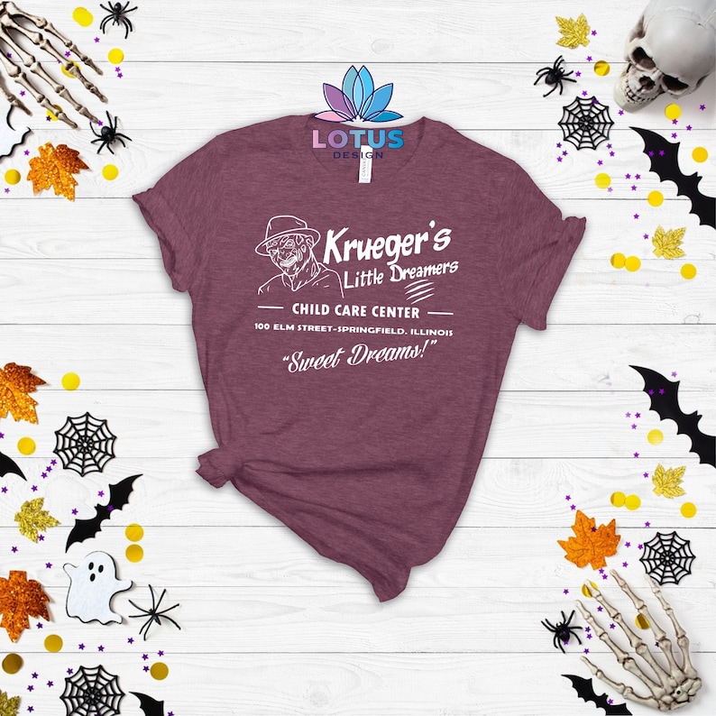 May include: A maroon t-shirt with a white graphic of a fictional character with a hat and a knife. The graphic says "Krueger's Little Dreamers Child Care Center 100 Elm Street-Springfield, Illinois "Sweet Dreams!"