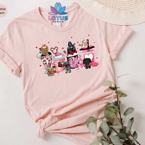 May include: A pink t-shirt with a graphic of Star Wars characters holding Valentine's Day themed drinks. The text "LOTUS DESIGN" is printed on the shirt.