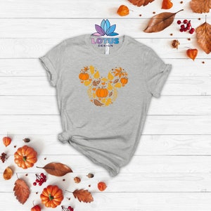 May include: A gray t-shirt with a fall-themed Mickey Mouse design featuring pumpkins, leaves, and hearts. The design is in shades of orange and yellow.