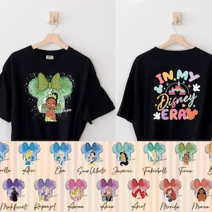 Puede incluir: Camiseta negra con un gr&aacute;fico de una princesa de Disney en una silueta de oreja de Mickey Mouse. La parte posterior de la camiseta tiene el texto "IN MY Disney ERA" con un castillo arco&iacute;ris y orejas de Mickey Mouse. Hay 10 opciones diferentes de princesas para elegir.