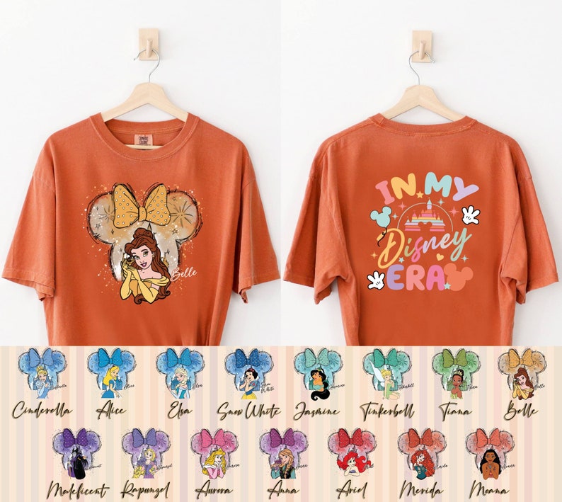 Puede incluir: Camiseta naranja con un gr&aacute;fico de Bella de La Bella y la Bestia en una silueta de oreja de Mickey Mouse. La parte posterior de la camiseta tiene el texto "In My Disney Era" con un gr&aacute;fico colorido del castillo de Disney. La camiseta est&aacute; disponible en 12 dise&ntilde;os diferentes de princesas Disney.
