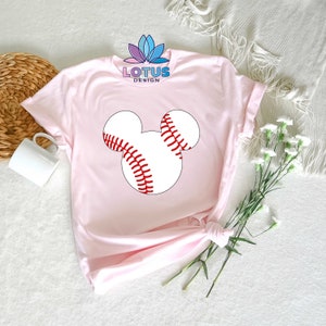May include: Pink t-shirt with a white baseball shaped like Mickey Mouse's head. The baseball has red stitching.