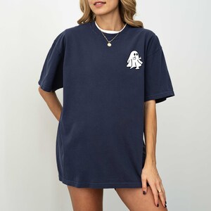 May include: A navy blue oversized t-shirt with a white ghost graphic on the left chest. The ghost has a friendly face and is giving a thumbs up.