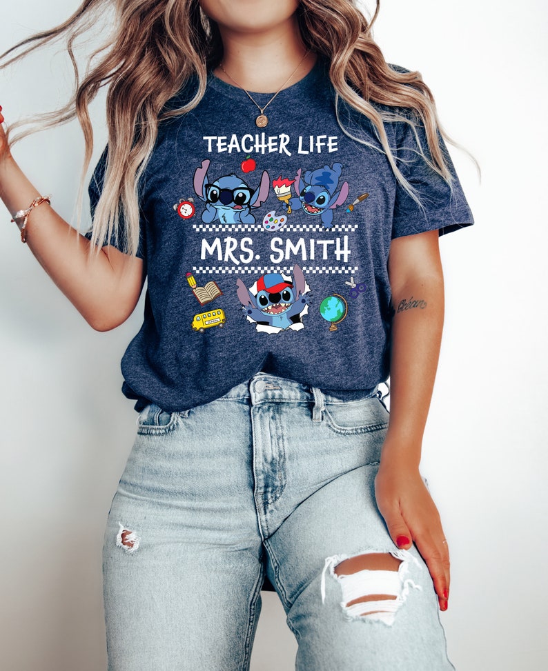 May include: A navy blue t-shirt with a white graphic of three Stitch characters from the Disney movie Lilo & Stitch. The characters are wearing school supplies and the text "Teacher Life" and "Mrs. Smith" is printed on the shirt.