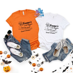 May include: Two white t-shirts with a vintage-style graphic design featuring a man in a hat and the text "Krueger's Little Dreamers Child Care Center 100 Elm Street Springfield, Illinois "Sweet Dreams!" "