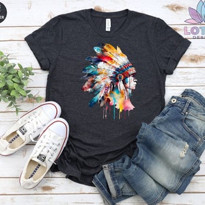 May include: A dark heather grey t-shirt with a watercolor illustration of a Native American headdress. The headdress is colorful with shades of blue, red, yellow, and green. The headdress is dripping with paint.