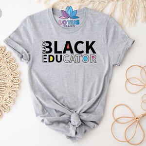 May include: A gray t-shirt with the text "I'm Black Educator" in colorful letters. The text is in a bold, blocky font.