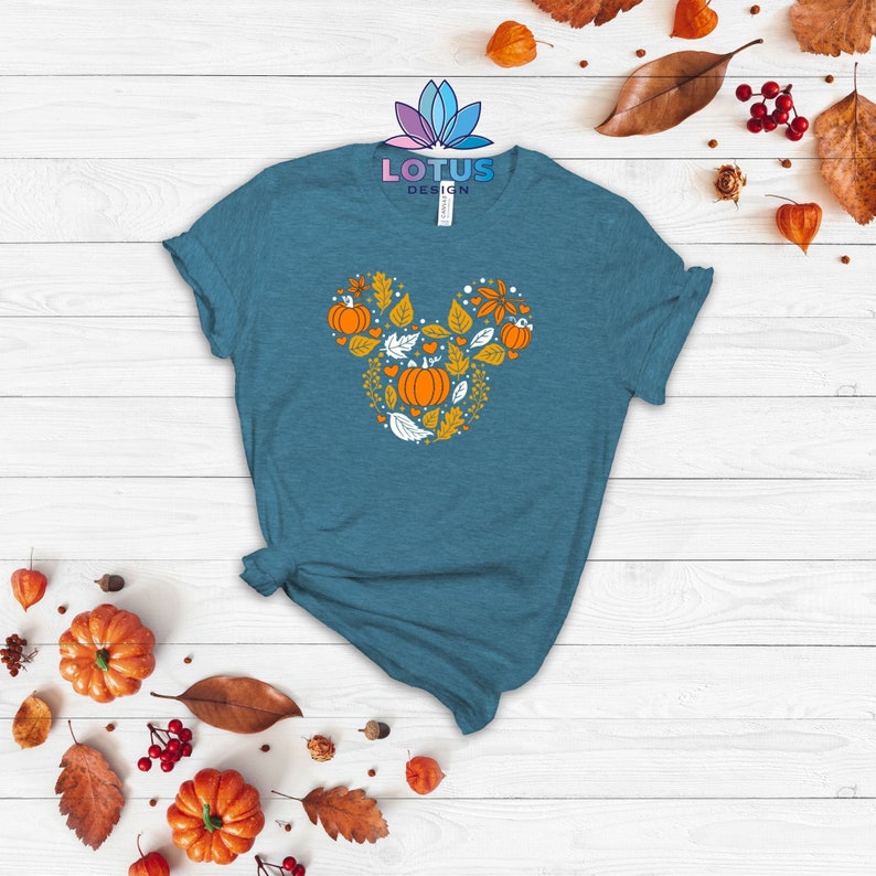 May include: A teal blue t-shirt with a white and orange Mickey Mouse head design featuring pumpkins and leaves. The design is centered on the shirt.