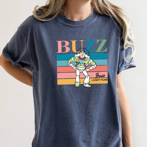 May include: A navy blue t-shirt with a retro-style graphic of Buzz Lightyear from Toy Story. The graphic features Buzz standing with his arms on his hips, and the text "Buzz Lightyear" is printed below him.
