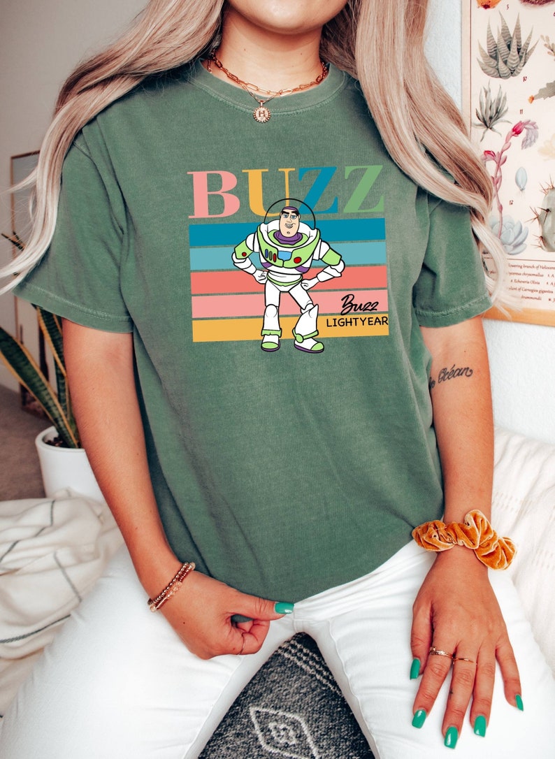 May include: Green t-shirt with a retro-style graphic of Buzz Lightyear from Toy Story. The graphic features Buzz in his space ranger suit with the text "Buzz Lightyear" underneath.