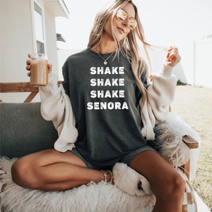 May include: A dark gray sweatshirt with the text "Shake Shake Shake Senora" printed in white on the front.