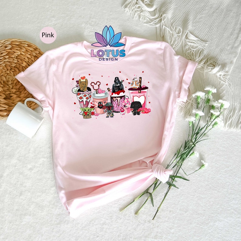 May include: Pink t-shirt with a graphic of Star Wars characters holding Valentine's Day themed drinks. The text "LOTUS DESIGN" is printed on the shirt.