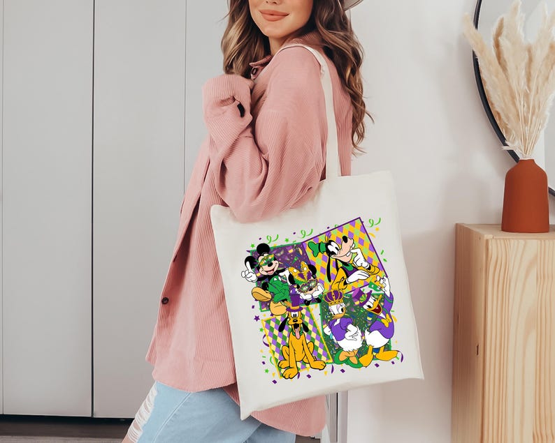 Puede incluir: Un bolso tote de color crema con un gr&aacute;fico colorido de Mickey Mouse, Minnie Mouse, Goofy, Donald Duck y Pluto con atuendos de Mardi Gras. El dise&ntilde;o incluye confeti y formas geom&eacute;tricas moradas, verdes y amarillas. El bolso tiene un dise&ntilde;o simple y resistente.