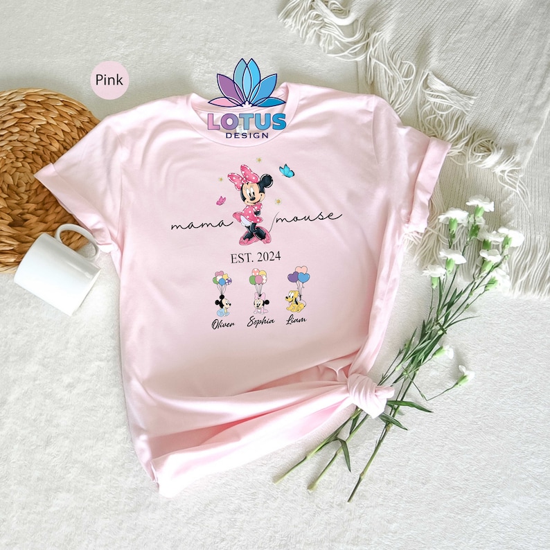 Puede incluir: Camiseta rosa con un gr&aacute;fico de Minnie Mouse sosteniendo globos con el texto "mama mouse EST. 2024" y los nombres "Oliver, Sophia, Liam" impresos debajo.