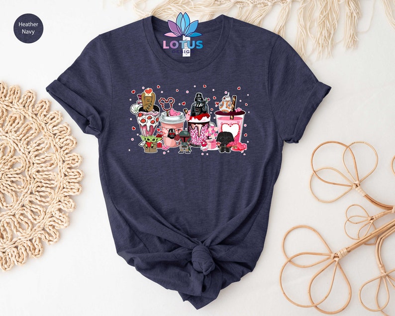 May include: A heather navy blue t-shirt with a graphic of Star Wars characters in pink Valentine's Day themed cups. The characters include Yoda, Darth Vader, Chewbacca, and R2-D2.