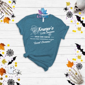 May include: A teal blue t-shirt with a white graphic design of a child care center called "Krueger's Little Dreamers". The graphic includes the text "Child Care Center", "100 Elm Street-Springfield, Illinois", and "Sweet Dreams!"