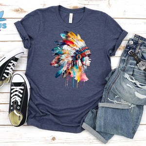 May include: A navy blue t-shirt with a watercolor illustration of a Native American headdress with colorful feathers. The headdress is dripping with paint.