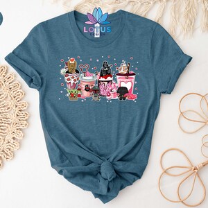 May include: A heather deep teal t-shirt with a graphic of Star Wars characters in Valentine's Day themed cups. The characters include Darth Vader, Yoda, Chewbacca, R2-D2, and a Stormtrooper.