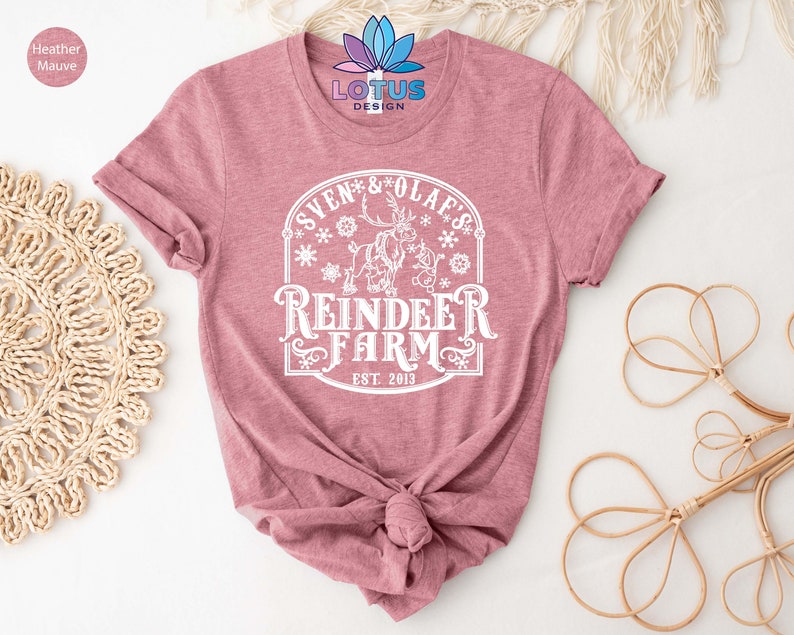 May include: A heather mauve t-shirt with a white graphic design featuring a reindeer and the text "Sven & Olaf's Reindeer Farm Est. 2013".