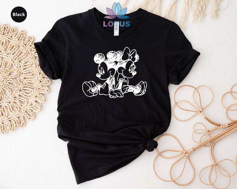 Pode incluir: Camiseta preta com um gr&aacute;fico branco do Mickey Mouse e da Minnie Mouse sentados juntos. O gr&aacute;fico &eacute; um estilo de desenho de linha simples.