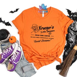 May include: Orange t-shirt with a black and white graphic of Freddy Krueger. The graphic says "Krueger's Little Dreamers Child Care Center 100 Elm Street-Springfield, Illinois "Sweet Dreams!"