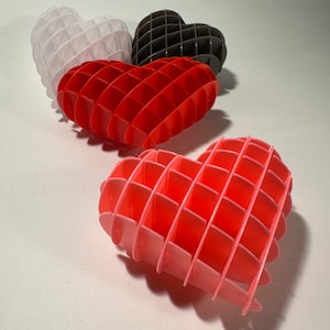 May include: Three heart-shaped decorations made of plastic, each with a different color: white, red, and pink. The hearts are made of a grid pattern of squares.
