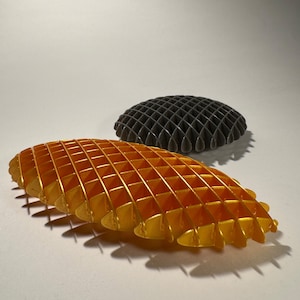 May include: Two geometric shapes, one gold and one black, with a grid pattern. The shapes are made of a 3D printed material.
