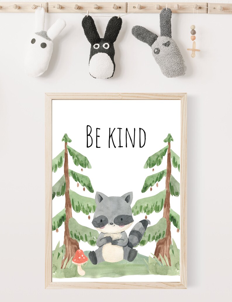 May include: A watercolor print with a cute raccoon sitting in a forest with two green pine trees and a red mushroom. The print has the text "BE KIND" in black lettering.