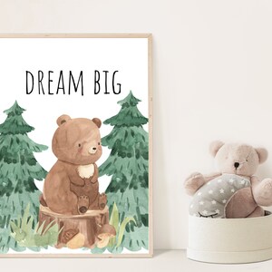 May include: A watercolor illustration of a brown bear sitting on a tree stump in a forest. The bear is surrounded by green trees and mushrooms. The text "DREAM BIG" is written in black at the top of the image.