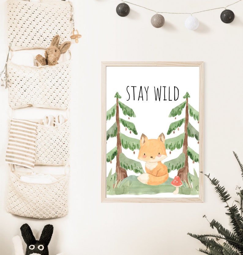 May include: A watercolor print featuring a cute fox sitting in a forest with the text "STAY WILD" above it. The print is framed in a light wood frame.