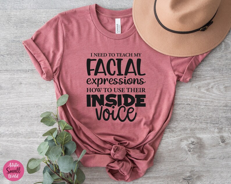 May include: A pink t-shirt with the text "I need to teach my facial expressions how to use their inside voice" printed in black.