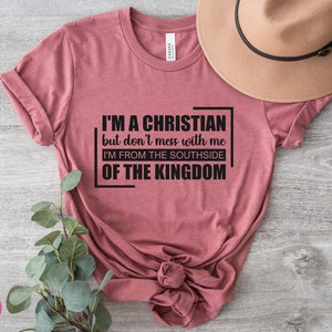May include: A maroon t-shirt with the text "I'M A CHRISTIAN but don't mess with me I'M FROM THE SOUTHSIDE OF THE KINGDOM" printed in black.