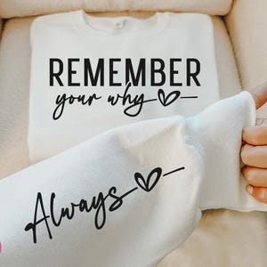 Puede incluir: Sudadera blanca con el texto "Remember your why" y un símbolo de corazón en la mitad superior y "Always" con un símbolo de corazón en la mitad inferior.