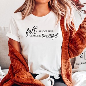 Puede incluir: Camiseta blanca con el texto "fall is proof that change is beautiful" en letras cursivas negras.