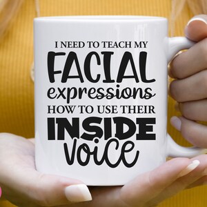 May include: White ceramic mug with black text that reads "I need to teach my facial expressions how to use their inside voice".