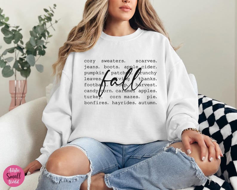 以下が含まれることがあります： 白いスウェットシャツに、大きな黒い文字で「fall」と書かれており、その周りを秋の言葉を並べたリストが囲んでいます。言葉には、居心地の良いセーター、スカーフ、ジーンズ、ブーツ、アップルサイダー、パンプキンパッチ、サクサクの葉、フットボール、感謝祭、収穫、キャンディーコーン、キャラメルアップル、ターキー、コーンメイズ、パイ、焚き火、馬車に乗る、秋などが含まれています。
