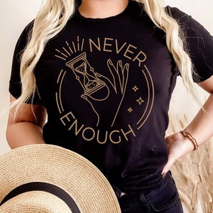 May include: Black t-shirt with a gold graphic of an hourglass and a hand with the text "NEVER ENOUGH" around it.