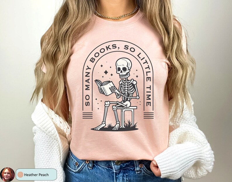 May include: A pink t-shirt with a graphic of a skeleton reading a book. The graphic is surrounded by an arch with the text "So Many Books, So Little Time".